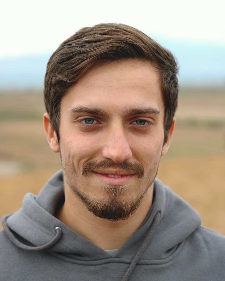 Symbolbild: ein lächelnder Mann im grauen Kapuzenpullover im Freien.