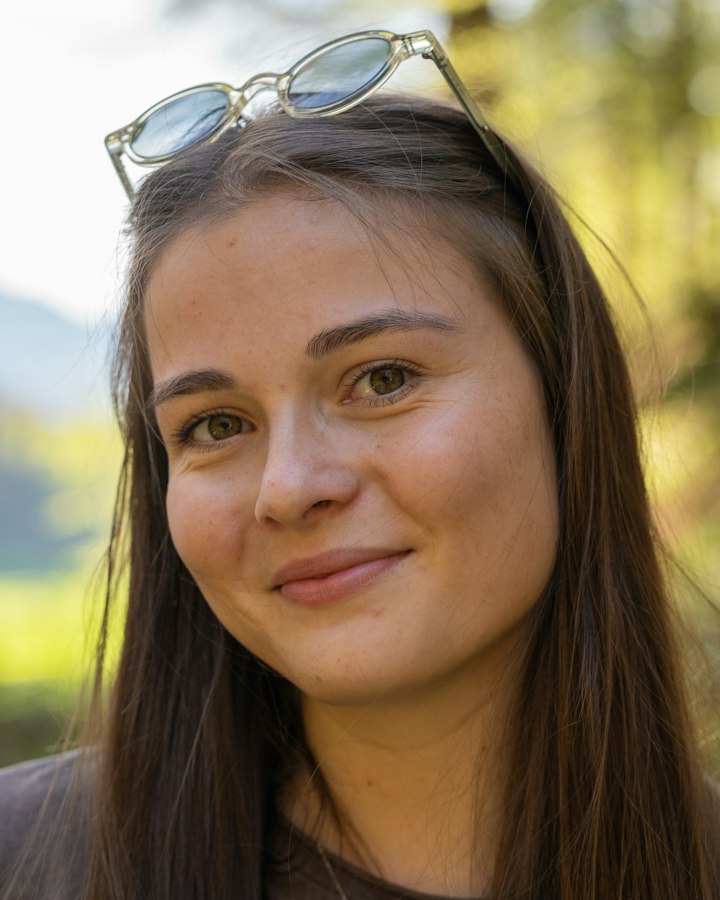 Symbolbild: eine Frau mit langen Haaren, die im Freien in die Kamera lächelt.